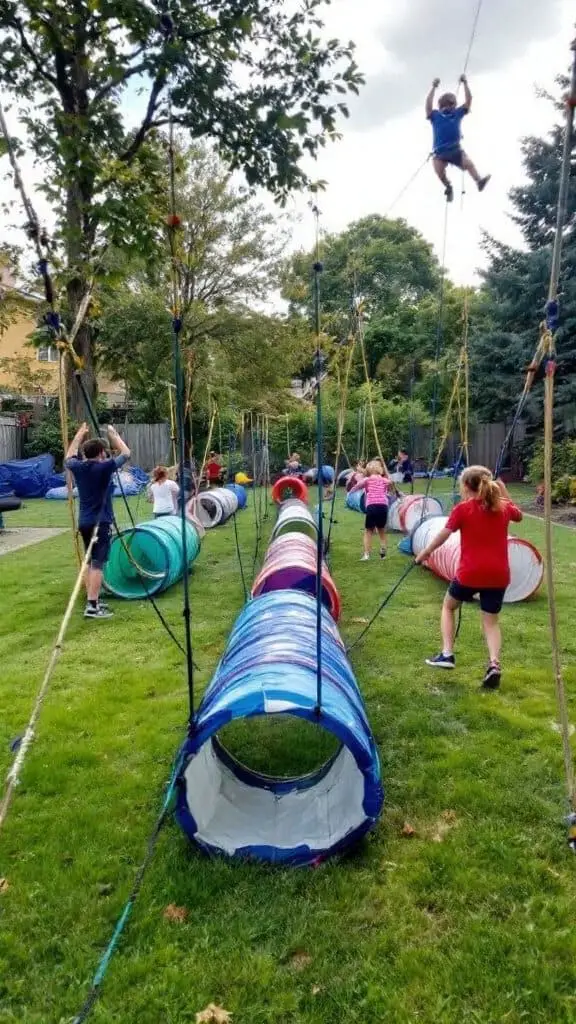 Children participating in an outdoor obstacle course with tunnels and ropes